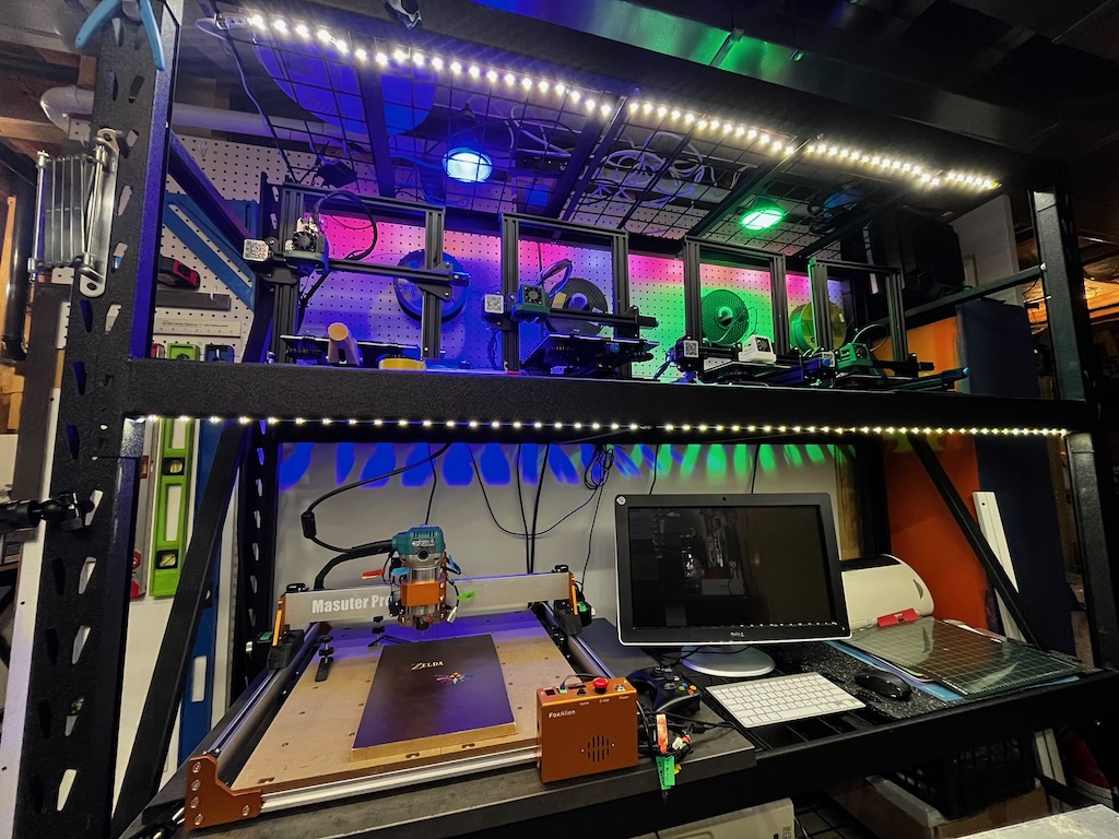 Maker workstation with printers, filament spools, and a CNC unit on a lit bench
